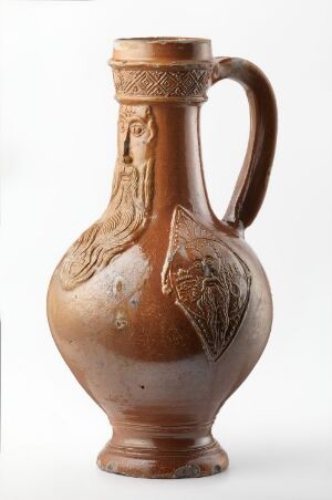  A traditional terracotta jug with an embossed band and relief work, featuring an ochre body with darker brown detailing near the rim and handle, set against a white background.