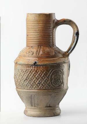  An ancient beige ceramic pitcher with a dark brown or black handle, featuring vertical ribbing on the upper half and intricate geometric patterns carved onto the lower half, against a light grey background. Artist name and title are unknown.