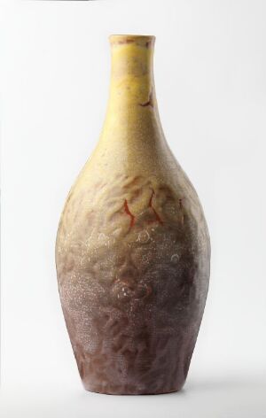  A tapering vase with a gradient of colors from yellow at the top through golden amber, earthy browns, muted purples, to sandy tones at the base, set against a neutral off-white background.