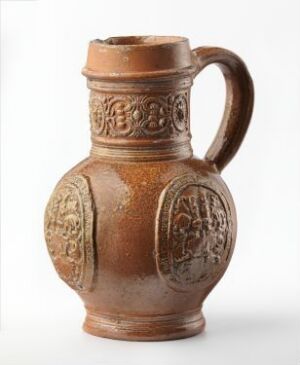  A terracotta jug with embossed medallion designs and a single handle, set against a neutral background, demonstrating historical craftsmanship and decorative artistry.