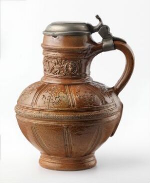  A traditional terracotta pitcher with a hinged metal lid and handle, featuring a central band of darker glaze adorned with etched decorative patterns, set against a light background.