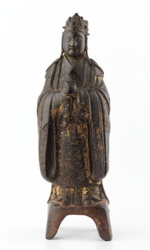  An intricate Eastern Asian statue of a serene figure in elaborate robes, featuring a detailed headdress and symbolic hand gestures, predominantly in dark brown with traces of gold, set against a white background. The figure seems to be made of aged bronze or wood and stands on a simple base. Artistname and title are unknown.