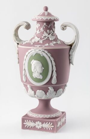  A neoclassical porcelain urn with a matte mauve or dusty pink color, featuring white relief decorations, intricate leaf patterns, swirled volutes on the handles, and a central oval cameo-like medallion in pale green with a white classical profile.