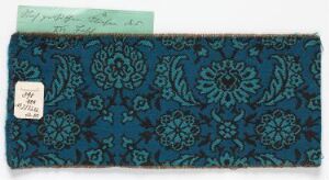  A rectangular piece of dark teal textile with darker, embossed-style floral patterns, accompanied by a small rectangular label and a larger label with handwritten text.