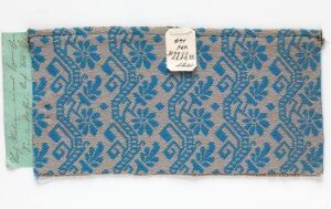  A teal and dark blue patterned fabric with a geometric diamond and star design, featuring a white identification label on the upper center part of the image.