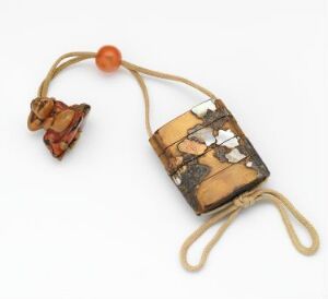  A photo of a tribal-style bone or ivory pendant with a pattern of black lines and spots, attached to a beige cord with a reddish-orange bead and a small, intricately carved animal figure, against a white background.