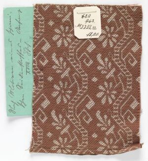  A small rectangular swatch of intricately patterned fabric in brown with lighter geometric designs, alongside a mint-green paper with handwriting, and a white label with hand-written numbering at the top right corner. Artist name and title remain unknown.