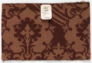  A rectangular sample of a patterned fabric in warm shades of brown, featuring a floral and foliate design, with a white inventory label attached to the top right corner.