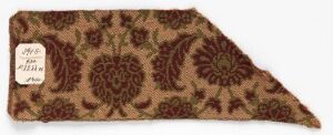  An asymmetrical trapezoidal fabric swatch with an intricate brown and maroon floral pattern, laid flat against a neutral background, featuring a small white square label.