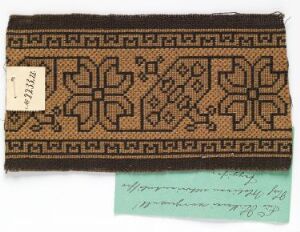  An intricately patterned brown and tan textile sampler with handwoven geometric and floral designs, accompanied by a handwritten numbered tag and a small green card with cursive text. Artist name and title unknown.