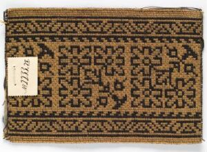  A photo of an aged rectangular textile fragment with a symmetrical geometric pattern in dark brown and black on a creamy beige background, featuring intricate designs and a white inventory tag on one corner.