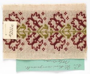  A small swatch of natural linen fabric with maroon and sage green embroidery of a floral and leaf design, with two labels attached showing handwritten numbers and text on a neutral background.