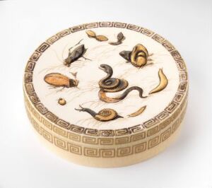  A circular off-white box with a lid, intricately decorated with snakes, nuts and seeds in brown and black tones, and a geometric border pattern.