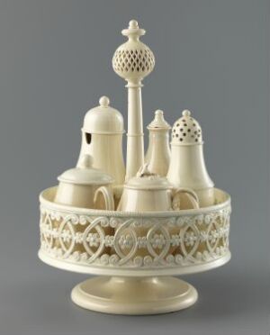  An intricately carved carousel made of creamy white material, possibly ivory, with a lacy midsection and miniature domed structures possibly serving as holders, all resting on a stout, rounded base.