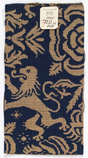  A vertical swatch of fabric featuring a golden stylized lion and floral patterns set against a dark navy blue background, with a label attached towards the top.