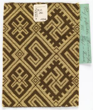  A piece of brown and beige geometric-patterned woven fabric with two labels attached, indicating a reference or catalog number.