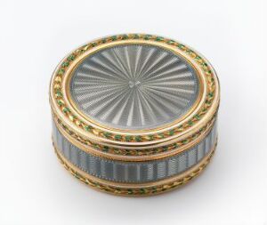  A luxurious circular box with a starburst patterned lid in silver and gray tones, and sides embellished with opulent bands of gold, blue with ridges, and inset jewels in green and red. The box conveys a sense of fine craftsmanship and decorative artistry against a plain white background. Artist name and title are unknown.