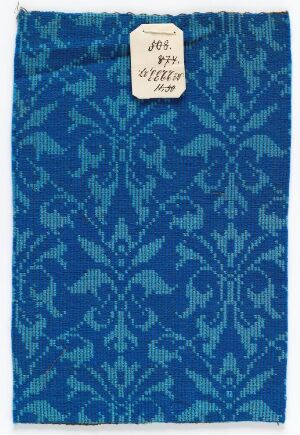  A rectangular fabric sample with a deep blue base and lighter blue ornate patterns, featuring a small white label attached in the upper right corner.