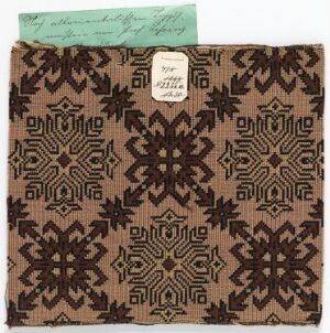  A patterned fabric square with a geometric design featuring stars and diamonds in shades of dark brown and black against a lighter brown background. Two labels, one attached by a string on the top left and another adhered in the center, suggest this might be a textile sample from a collection.