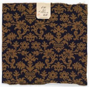  A square piece of fabric with a dark blue background and elaborate gold motifs, featuring a tag in the upper right corner. The design has a historical or traditional aesthetic, suggesting it may be used for ornate decoration or fashion.