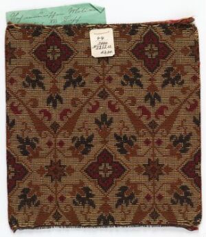  A fragment of an historical textile with a symmetrical pattern featuring diamond shapes and stylized botanical elements in colors of deep brown, beige, dark red, and subdued blue, with frayed edges and an attached archival tag in the top left corner.