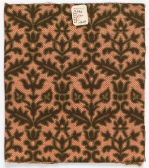  A square textile sample with a repeating pattern of intricate black and dark brown botanical motifs on a salmon-pink background, featuring a museum inventory tag in the top right corner.