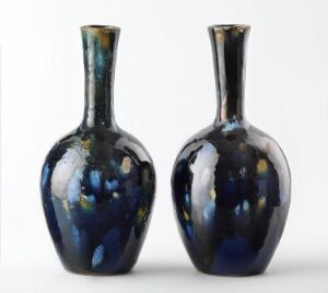  Two ceramic vases with a deep blue glaze and iridescent spots of green, yellow, and cobalt blue, set against a light grey background.