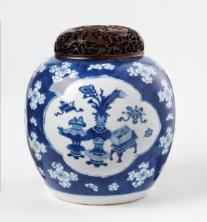  A traditional blue and white ceramic jar with a rounded body, featuring symmetric floral and vase motifs, and a dark brown intricately carved lid on top.