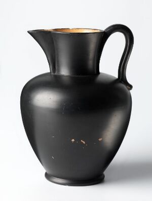  A black, bulbous pitcher with a golden interior, a graceful handle, and a spout on a plain light background. The jug displays signs of light wear with a few spots where the black surface has chipped away. Artist name and title are unknown.