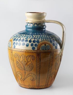  A ceramic jug with a glossy finish, featuring a cobalt blue upper half with white dot patterns and a terracotta lower half with hand-painted vine motifs. The jug has a flared rim and a single handle, set against a plain background. Artistname and title are unknown.