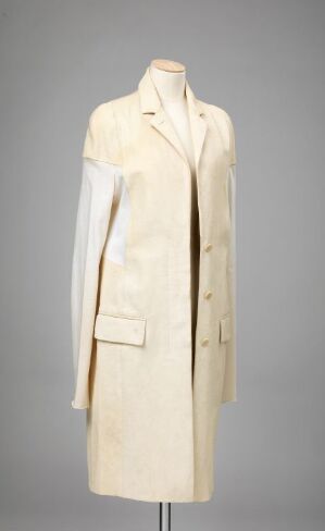  A long, single-breasted coat in an off-white color by Helmut Lang displayed on a mannequin against a gray background, tailored from a fine cotton fabric and featuring a classic notched collar, matching buttons, and discreet pockets, conveying a sense of minimalist elegance.