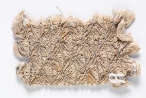  A textured fragment of antique lace with intricate geometric patterns in light beige, featuring frayed edges against a white background. Artist name and title are unknown.