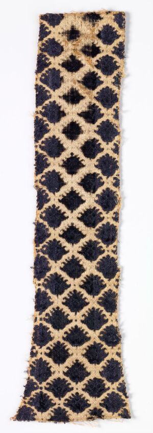  A long, narrow textile strip with a cream-tan background featuring a repeating pattern of diamonds outlined in gold, filled alternately with navy blue and dark purple-black colors, suggesting a luxurious and ornate design.