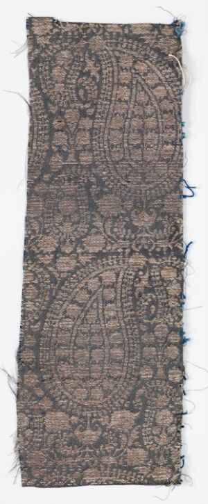  A long, narrow antique textile fragment with a detailed, symmetrical pattern in muted brown tones, showing signs of wear and age with frayed edges and a lightly textured surface.