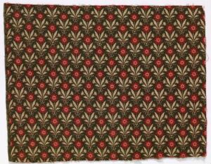 
 A patterned textile featuring a repeating motif of small red flowers with four petals each, surrounded by green foliage against a warm brown background. The design is symmetrical and seamless, suggesting a decorative fabric or wallpaper with a balancing combination of reds and greens.