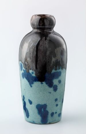  A ceramic vase with a tapering cylindrical shape, featuring a glossy black glaze dripping over the top half and transitioning to a mint background with cobalt blue splashes on the lower half, set against a light background.