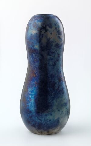  An upright, smooth, three-dimensional object resembling a gourd or stylized figure with a narrow waist, displaying a glossy surface that features deep blues, blacks, subtle greens, with specks of white and hints of rust red and burnt orange, set against a neutral light grey background.