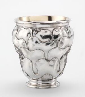  A reflective, silver-colored vase with an organic, fluid design featuring bulbous shapes and indents, suggestive of molten metal, set against a neutral background. Artist name and title are unknown.