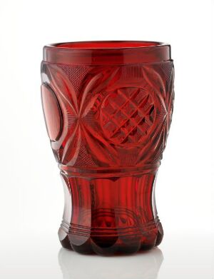  A deep red cut-crystal glass with a tapered shape and elaborate patterns of diamonds and curves that catch the light, set against a clean, white background.