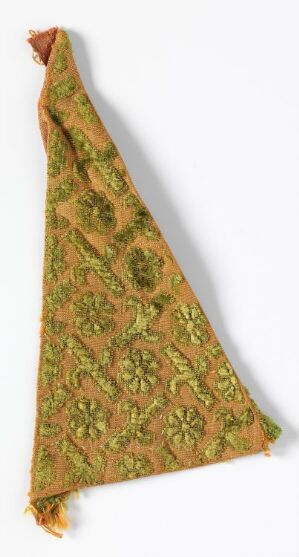  A folded triangular piece of fabric with an intricate pattern in hues of green and yellow, accented with orange and brown, suggesting a vintage or decorative textile.