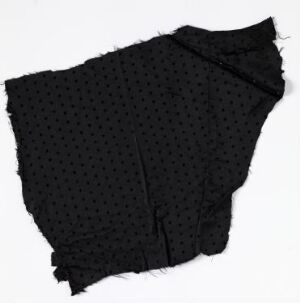  A piece of black fabric with a textured, raised polka-dot pattern, showing uneven and frayed edges against a light background.