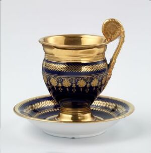  Decorative cup with a golden rim and handle, and a deep blue body with golden detailed patterns, accompanied by a matching saucer, all set against a neutral background.