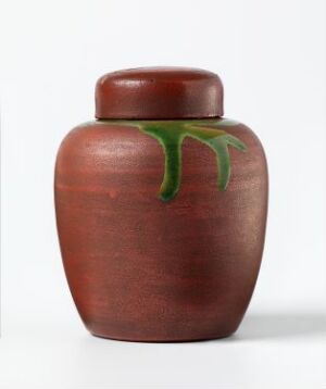  A deep red ceramic jar with a rounded body and a separate lid on a white background. The jar features an organic green drip glaze decoration just below the lid. Artist name and title are unknown.