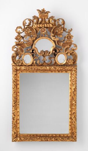  An antique, vertically oriented ornate mirror with a glossy golden frame featuring a decorative crown at the top and symmetrical leaf or floral motifs throughout, accompanied by rounded elements and elaborate scrollwork.