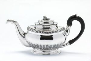  A shiny silver teapot with an ornate design and a black handle on a stark white background.