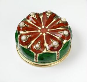  A small, circular box with a domed lid, featuring a red and green floral design accentuated with pearl-like elements and gold outlines.