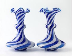  A pair of white glass vases with deep blue swirling patterns, featuring elongated forms with ruffled rims atop a flat base, displaying a dynamic and artistic design.