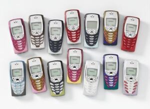  A collection of 16 vintage Nokia mobile phones, designed by the Nokia Design Team, displaying a variety of colors including blue, red, silver, and gradient designs, arranged loosely in a grid on a white background.