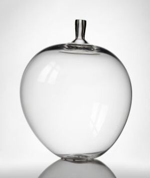  "Eplet," a clear blown glass apple designed by Orrefors Glasbruk A/B, demonstrates the craftsmanship of glassblowing with its simple, elegant form against a white background.