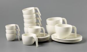  A collection of white glazed porcelain tableware designed by Stefan Lindfors, including cups with saucers and shallow bowls or plates, displayed against a neutral grey background.